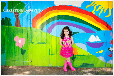 Beautiful girl in pink tutu leaning against a colorfully painted rainbow wall