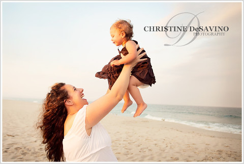 Beautiful mom holding baby daughter in the air on the beach along the ocean