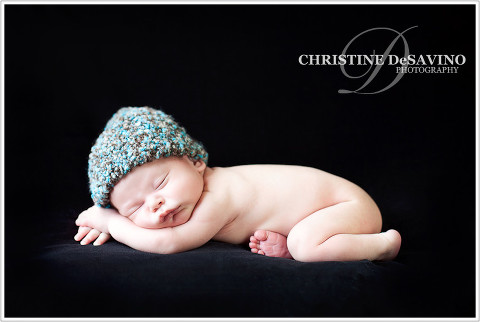 Angelic newborn boy sleeps on black background with blue knit hat