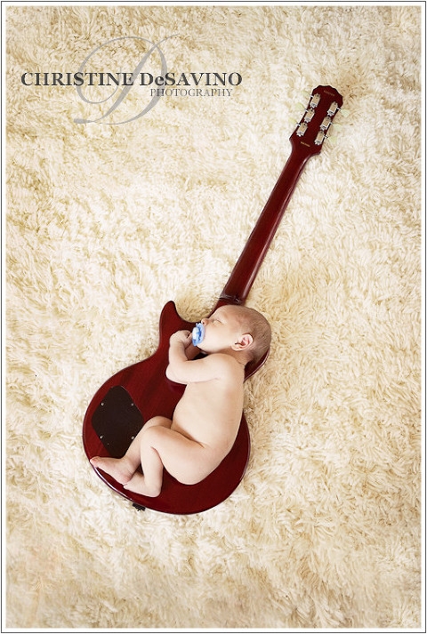 Infant boy with pacifier sleeping on guitar