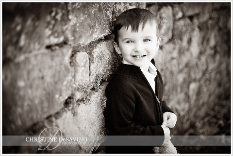 Black and white image of boy leaning against stone wall smiling - NJ Child Photographer