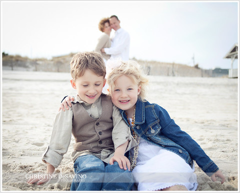 Brother and sister on beach with parents in background - NJ Family Photographer