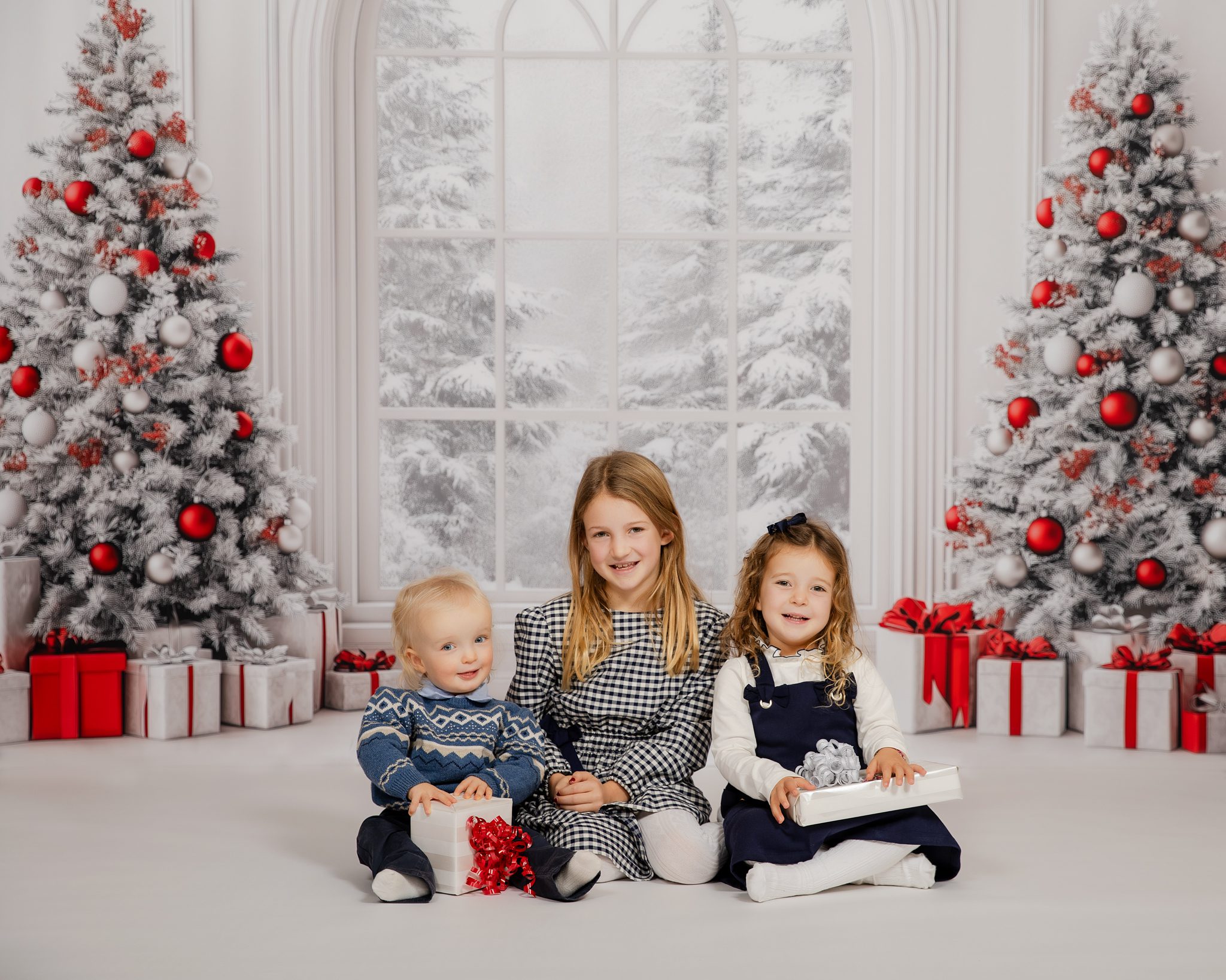 Three young children smiling in festive holiday mini session with Christmas trees and gifts, Bergen County NJ