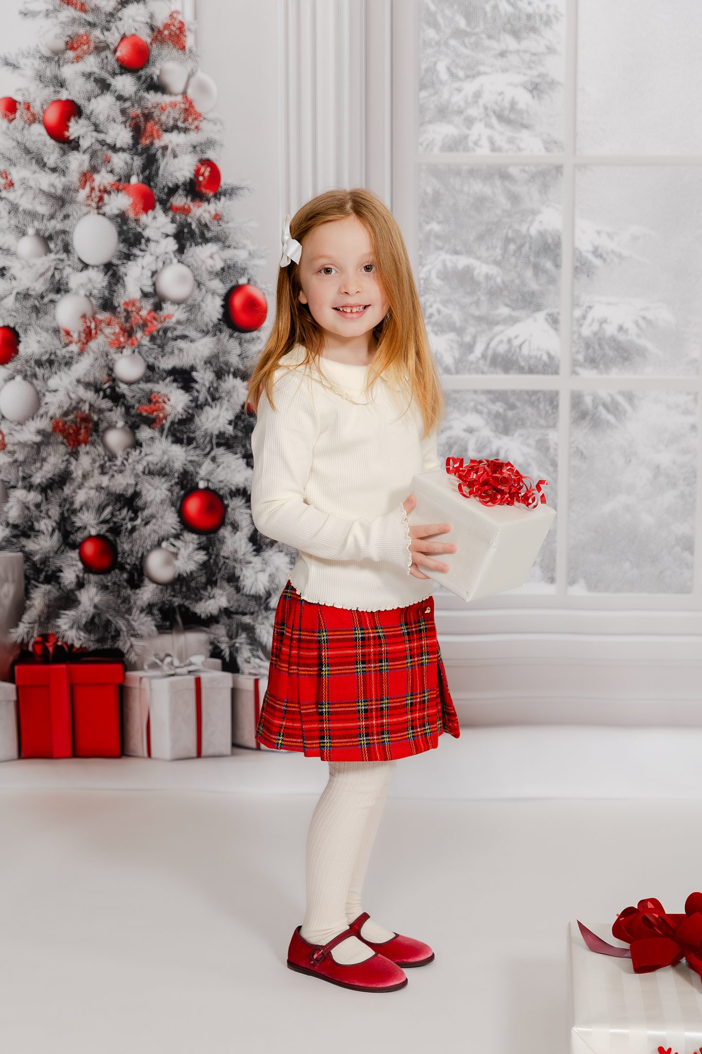Girl in red plaid skirt holding a holiday gift during Christmas mini session in Bergen County NJ